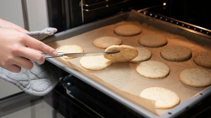 A tray of cookies coming out of the oven.  Someone is lifting one cookie to check if the bottom is ready.