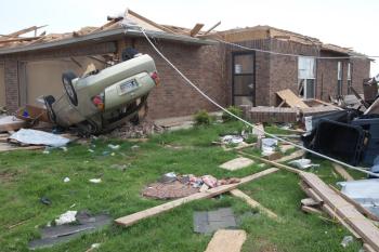 A car turned upside down by an F5 tornado that hit Moore, OK in 2013.  The picture also shows major damage to a house, and major debris littered around the yard.